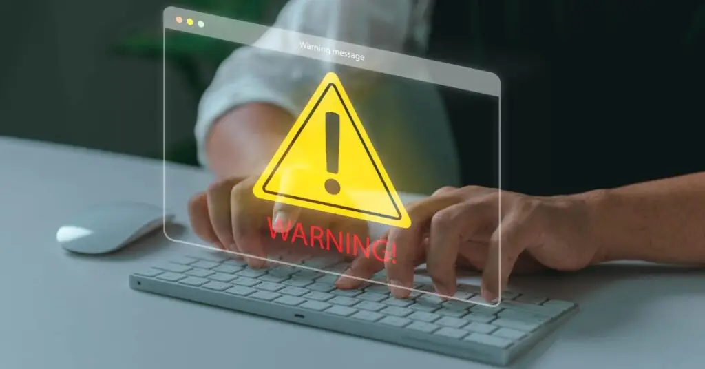 A person typing on a computer keyboard with a transparent warning notification showing a yellow triangle with exclamation mark, illustrating how macros pose a cybersecurity risk through real-world examples like NotPetya that triggered security alerts for affected organizations.